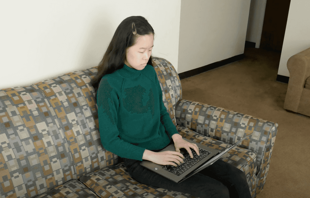 a person sits on a couch typing on a laptop